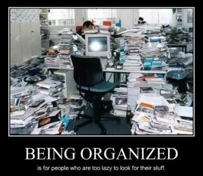 Meme, un bureau dans un open space est entouré de montagnes de dossiers papiers, le texte est : being organized is for people who are too lazy to look for their stuff